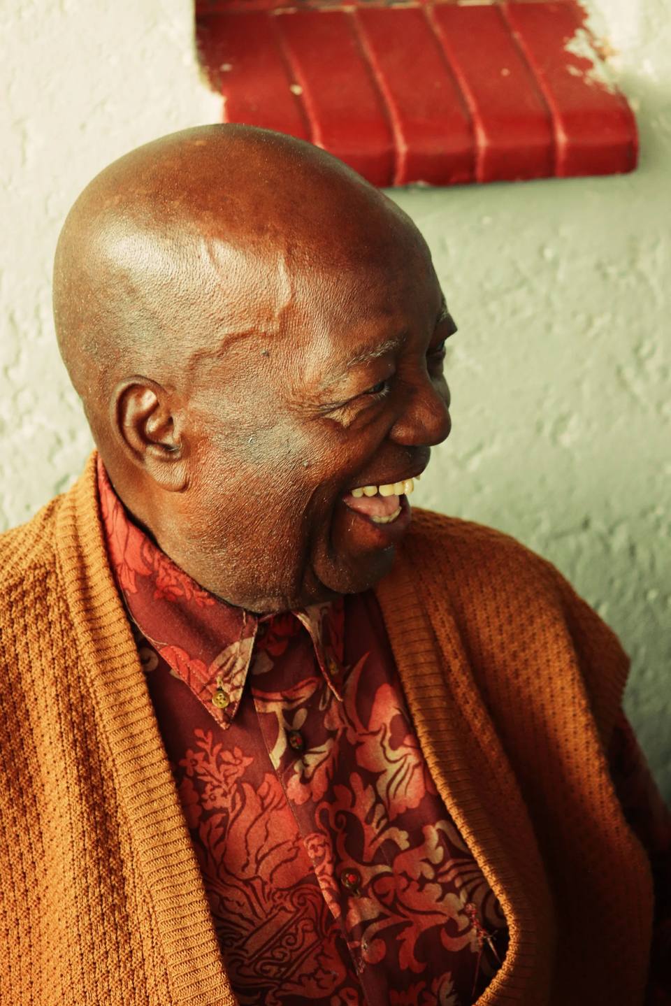 A smiling man in a brown cardigan and red patterned shirt